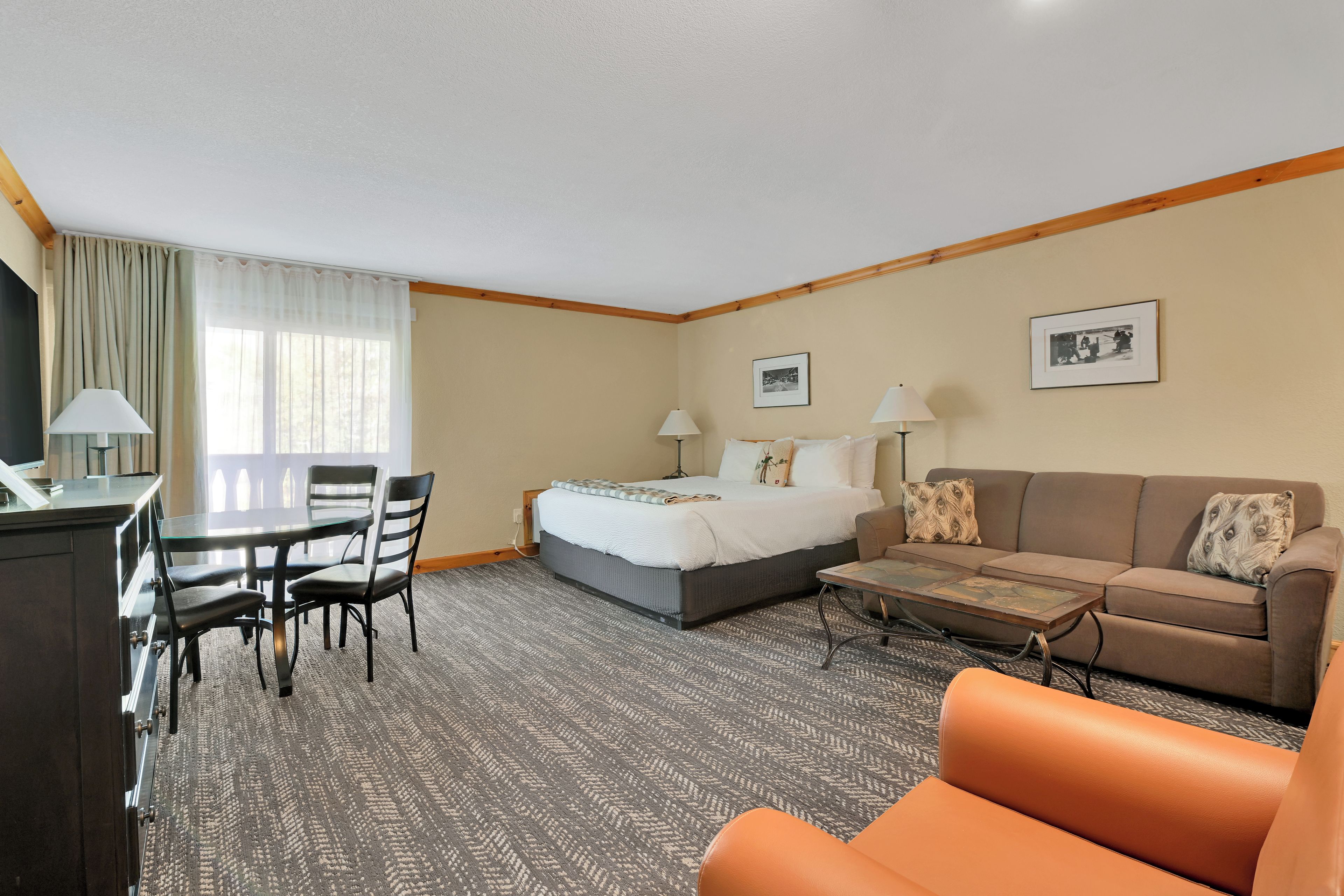 A hotel room with a bed, a sofa, a coffee table, a desk with chairs, and a television.