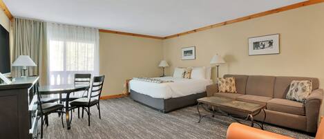 A hotel room with a bed, a sofa, a coffee table, a desk with chairs, and a television.