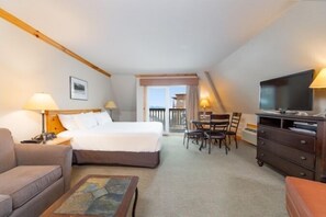 A hotel room with a bed, a desk, a television, a sofa, and a view of the outside. - Selkirk Lodge (Sandpoint)