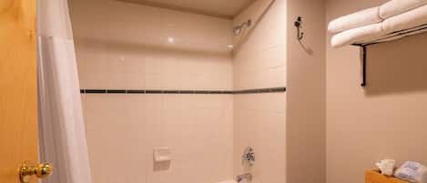 Een badkamer met een badkuip, douche en toilet. Handdoekrek met handdoeken en een verzorgingsset.