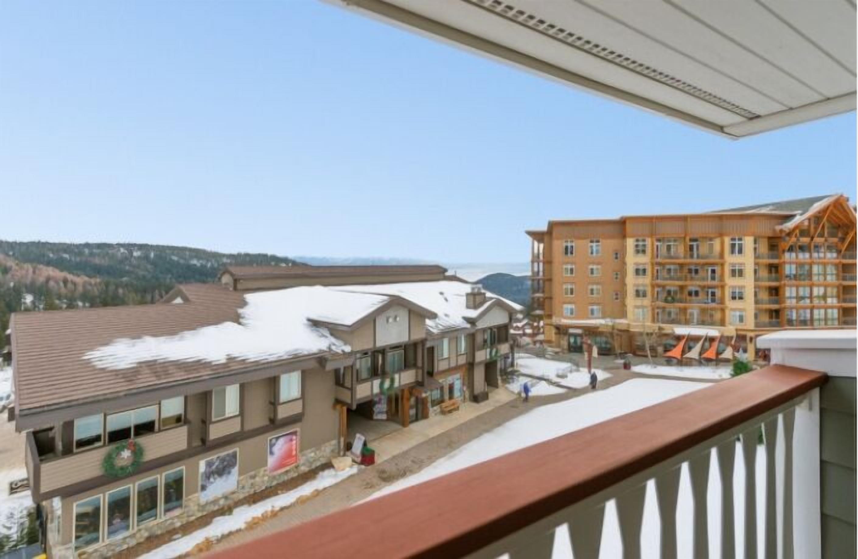 A multi-story building with a snow-covered roof, a balcony with a railing, and a view of a mountainous landscape.