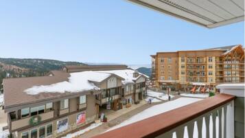 A multi-story building with a snow-covered roof, a balcony with a railing, and a view of a mountainous landscape.