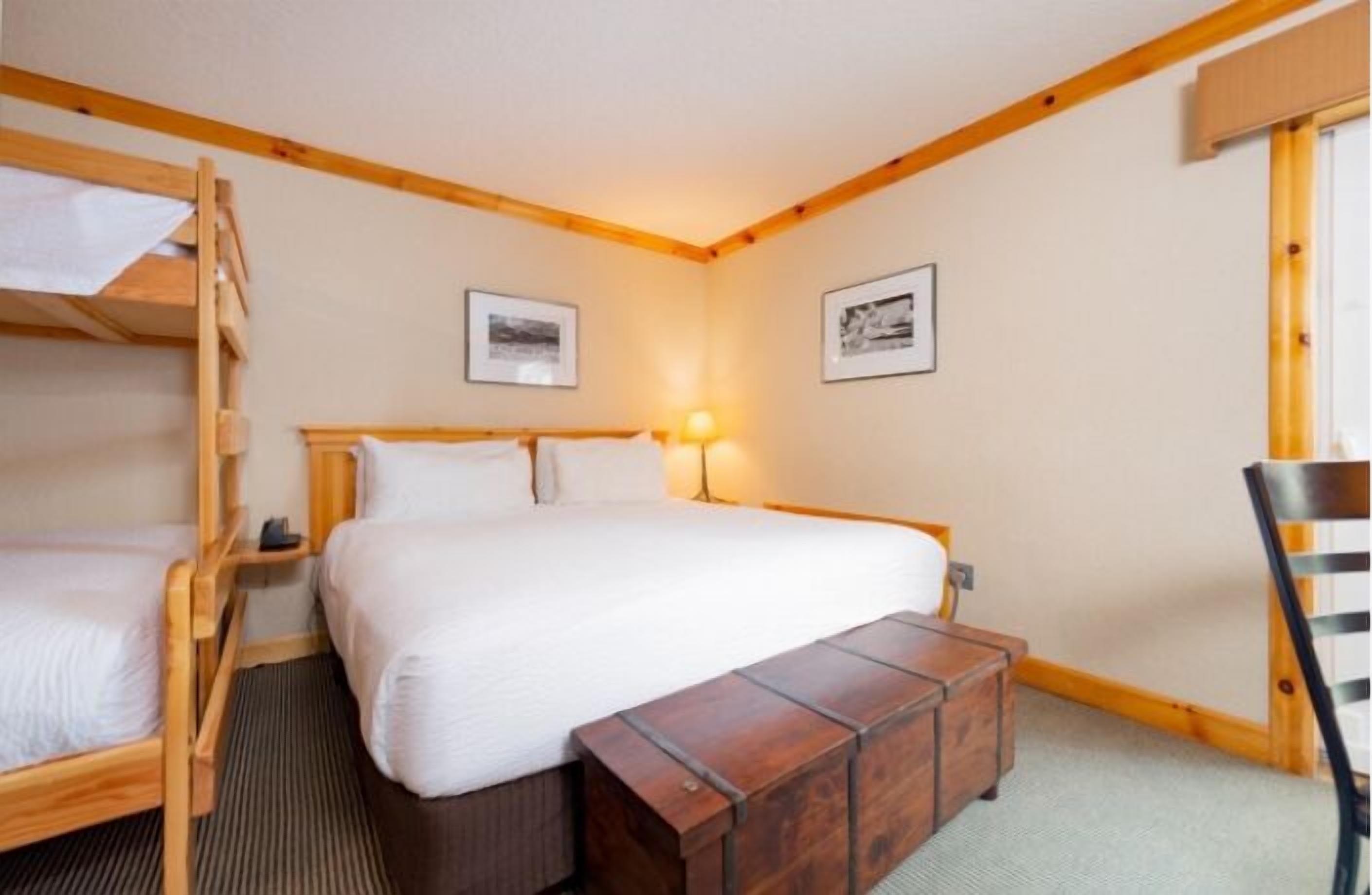 A room with a bunk bed, a single bed, a wooden bench, and two framed pictures on the wall.