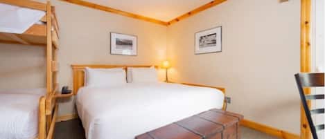 A room with a bunk bed, a single bed, a wooden bench, and two framed pictures on the wall.