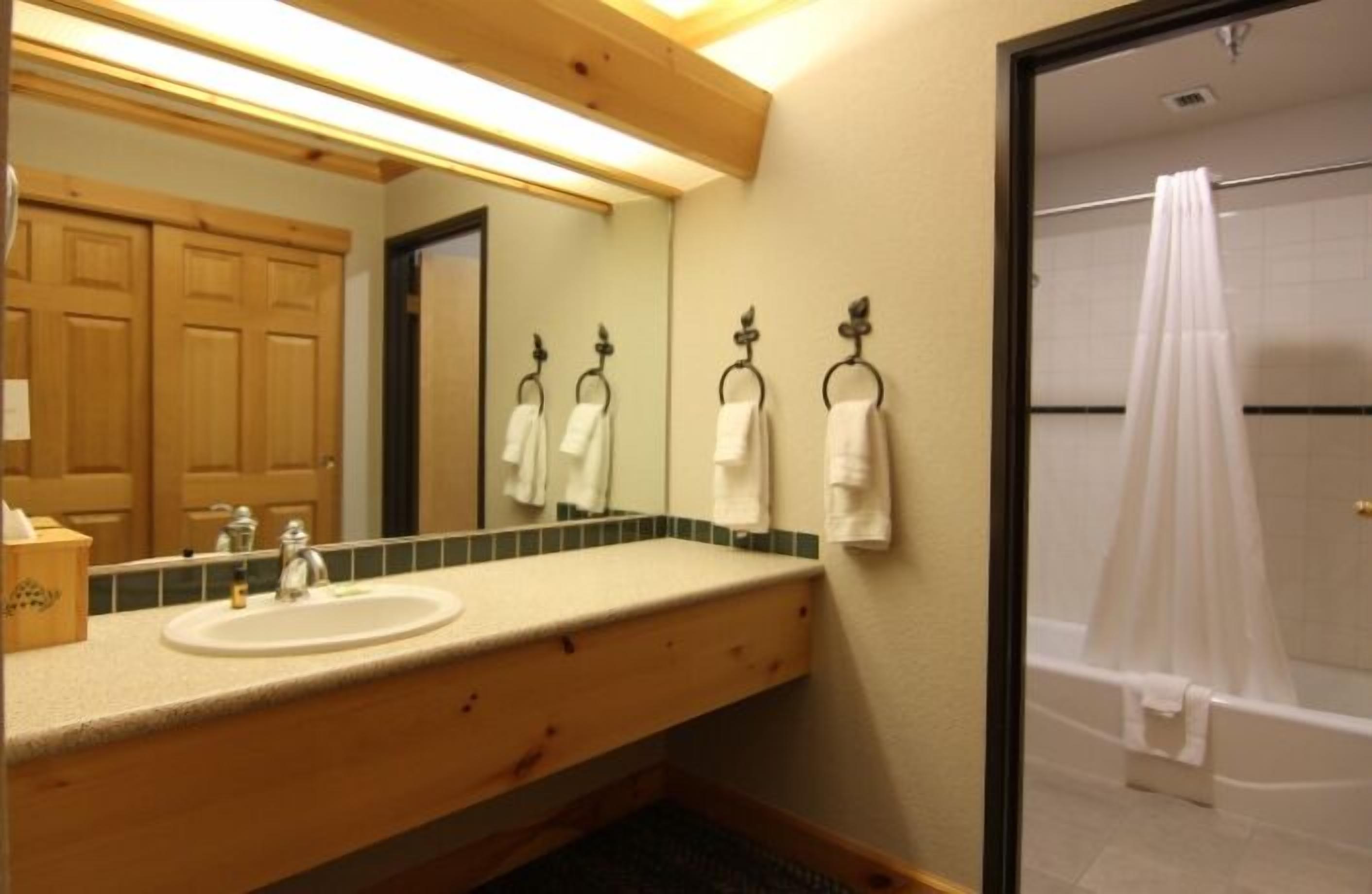 A bathroom with a wooden vanity, a sink, a mirror, and a shower with a curtain.