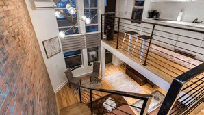 Un interior de varios niveles con una escalera, una zona de cocina y vistas a un edificio industrial.