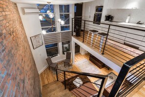 Ambiente interno su più livelli, con una scala, angolo cottura e vista su un edificio industriale.