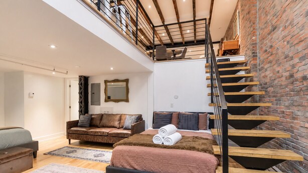 Un dormitorio estilo loft con una escalera de madera, un sofá, una cama y un espejo grande.