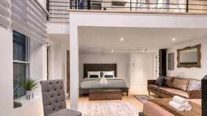 Un interior moderno con una cama, un sillón gris, un sofá marrón y un espejo grande.