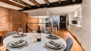 Un comedor con pared de ladrillo, una mesa redonda preparada para cuatro personas y una botella de vino.