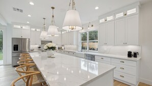 A modern kitchen with a large island, white cabinetry, and a stainless steel refrigerator. - Luxury Villa with Huge Kitchen/ Hot Tub/ Barrel Sauna (Boerne)