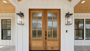 A double wooden door with frosted glass panels, flanked by two black lantern-style lights, set in a white paneled wall with a wooden ceiling. - Luxury Villa with Huge Kitchen/ Hot Tub/ Barrel Sauna (Boerne)