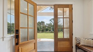 A wooden door with glass panels leading to a patio with a lawn and trees. - Luxury Villa with Huge Kitchen/ Hot Tub/ Barrel Sauna (Boerne)