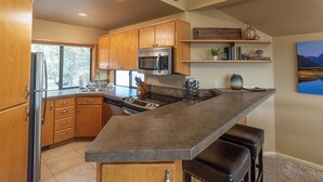 Una cocina moderna con armarios de madera, un refrigerador de acero inoxidable, un microondas y una isla grande con taburetes de bar.