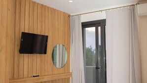 Ein modernes Schlafzimmer mit einer Holzwand, einem Flachbildfernseher, einem runden Spiegel, einem Bett mit weißer Bettwäsche und einer Schiebetür mit Vorhängen.