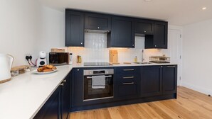 Une cuisine moderne avec des meubles de couleur sombre, un four encastré et un plan de travail blanc.
