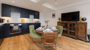 Une cuisine moderne avec des meubles de couleur sombre, un four encastré et un coin repas comprenant une table ronde et des chaises.
