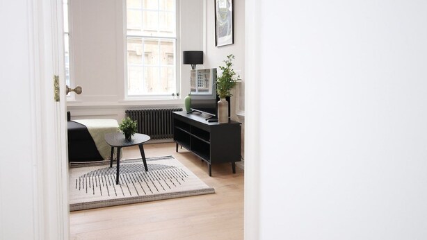 A modern living room with a sofa, a small table, a black TV stand, and a radiator.