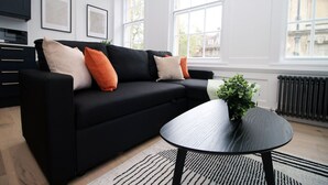 A modern living room with a black sofa, a round black coffee table, and a patterned rug.