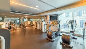 Ein Fitnessstudio mit verschiedenen Trainingsgeräten, einem großen Spiegel und einem Fernseher an der Wand.