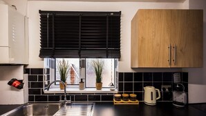 A kitchen with a black countertop, stainless steel sink, wooden cabinets, a window with black blinds, and a potted plant. - Spacious 4 Bed with Free Parking (Southampton)