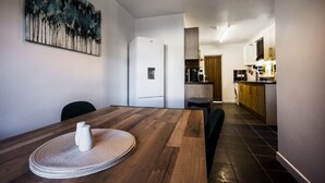 A modern kitchen with a wooden table and chairs, a painting on the wall, and a view into the dining area. - Spacious 4 Bed with Free Parking (Southampton)