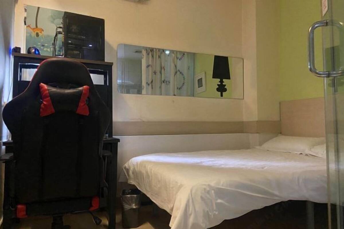 Una habitación de hotel con una cama, un escritorio con computadora, una silla, un espejo y una lámpara.