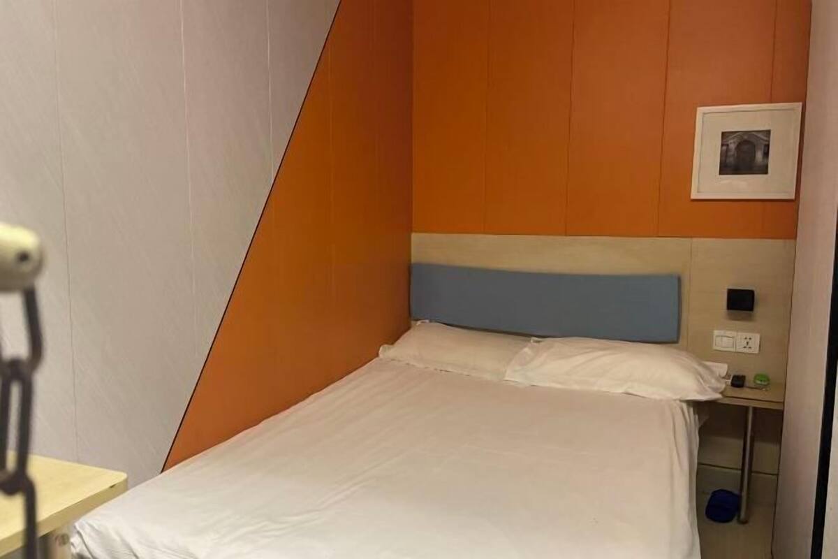 Habitación de hotel con cama, mesita de noche, cuadro colgado en la pared y toma de corriente.