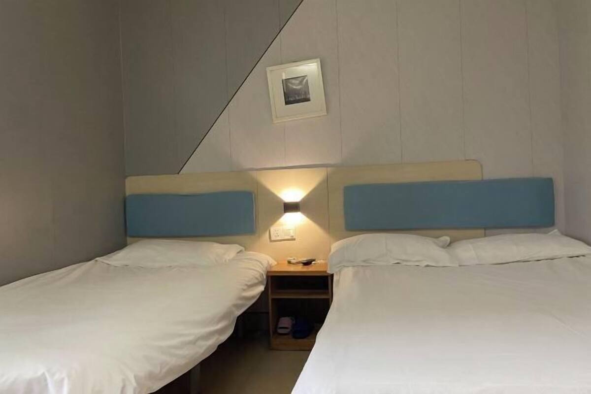 Habitación doble con dos camas, una mesita de noche con lámpara y un estante pequeño con pantuflas.