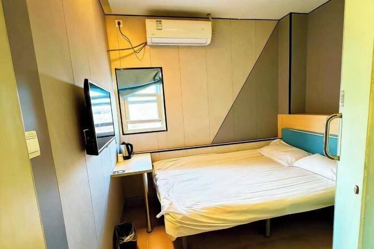 Habitación de hotel pequeña con una cama individual, un escritorio, televisión y aire acondicionado.