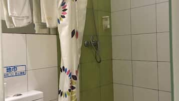 A bathroom with a toilet, a shower with a green tiled wall, and a curtain with a colorful leaf pattern.