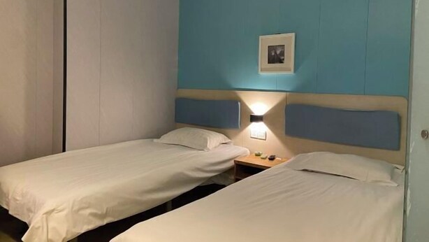 Een hotelkamer met twee eenpersoonsbedden, een nachtkastje met een lamp en een lijst aan de muur.