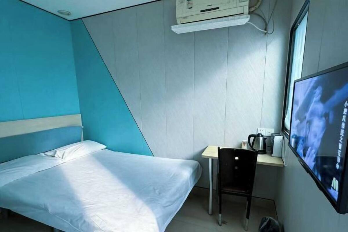 Una habitación con cama, escritorio, silla, televisor y aire acondicionado.