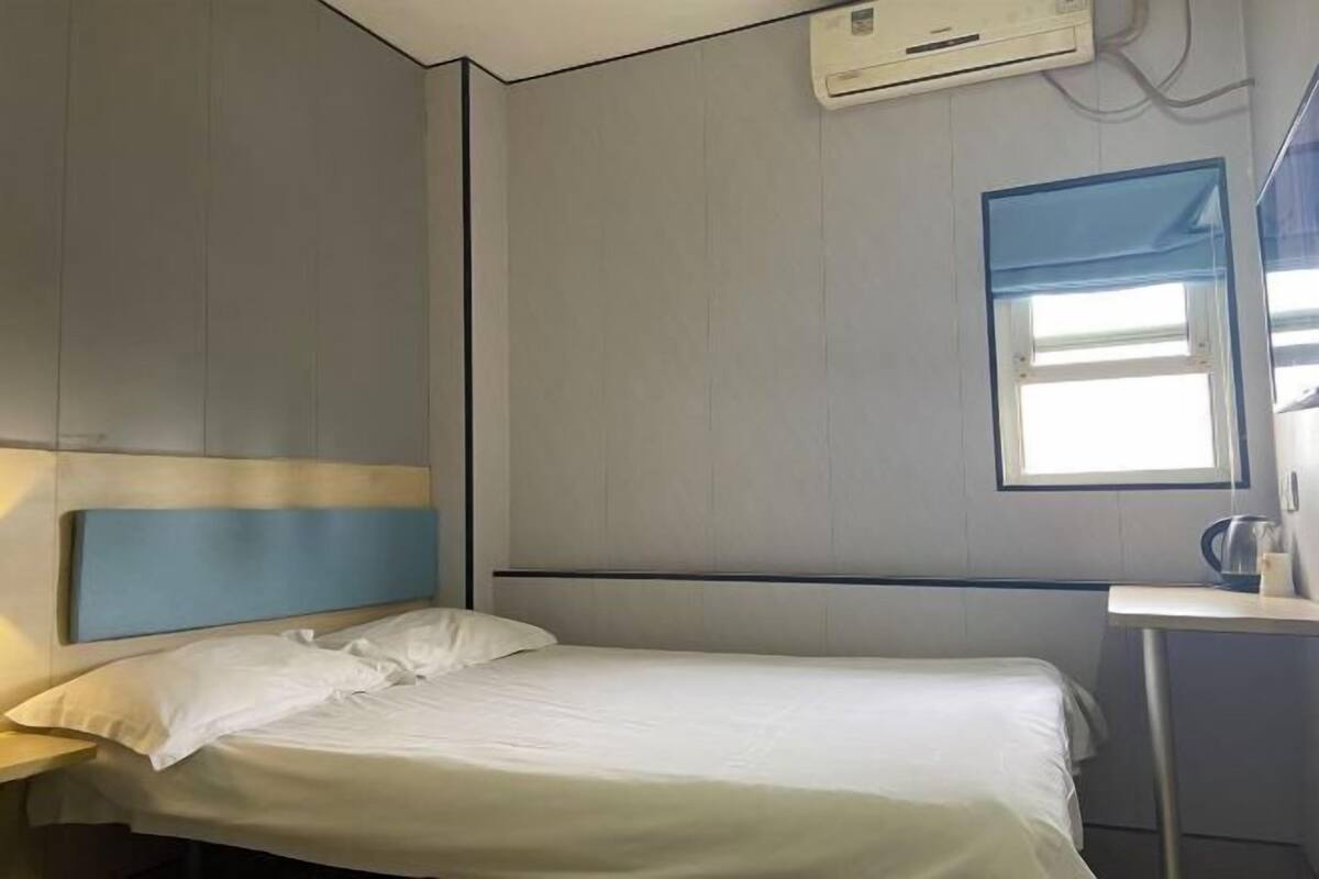 Una habitación de hotel con una cama, una mesita de noche, una ventana y un equipo de aire acondicionado.