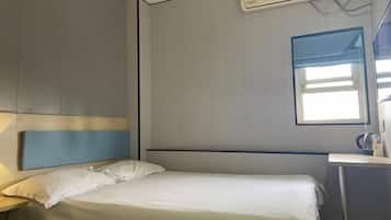 A hotel room with a bed, a nightstand, a window, and an air conditioning unit.
