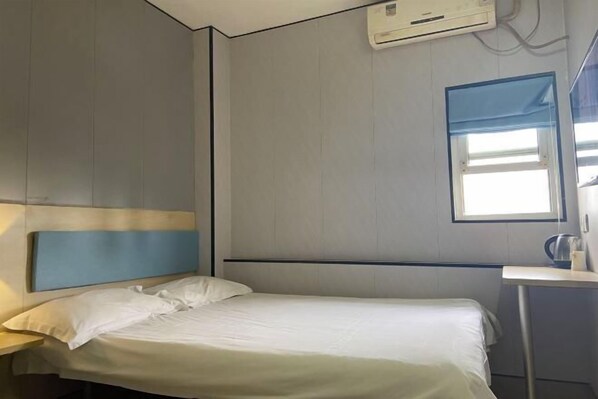 A hotel room with a bed, a nightstand, a window, and an air conditioning unit.