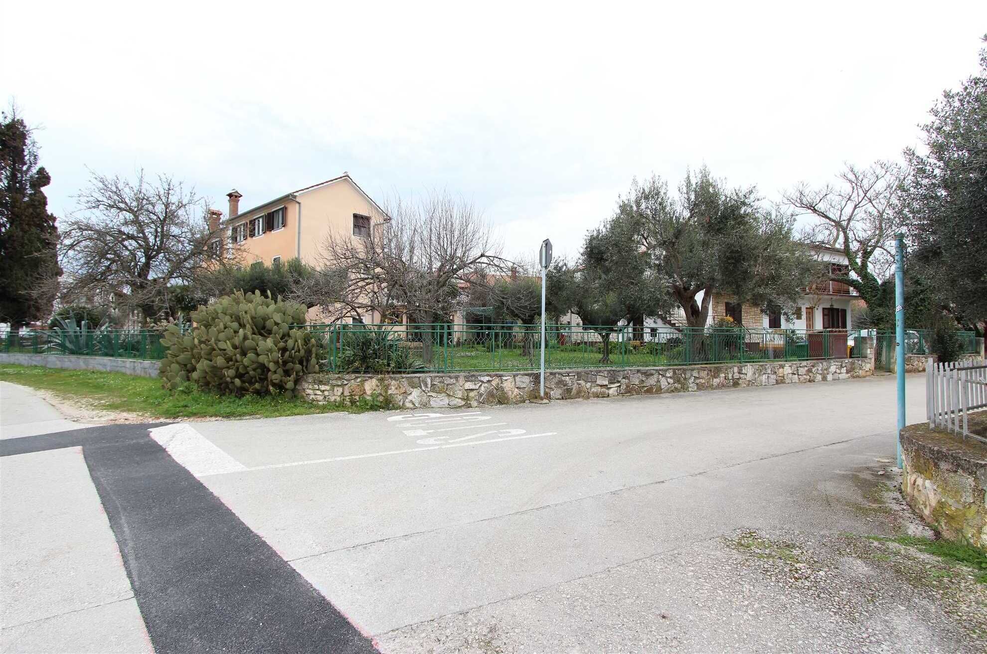 Una calle tranquila con acera, una valla verde y edificios al fondo.