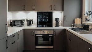 Et moderne køkken med mørke skabe, mikrobølgeovn, komfur og kaffemaskine.