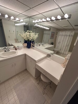 Un baño moderno con tres lavamanos, un espejo grande con iluminación y un jarrón con flores.