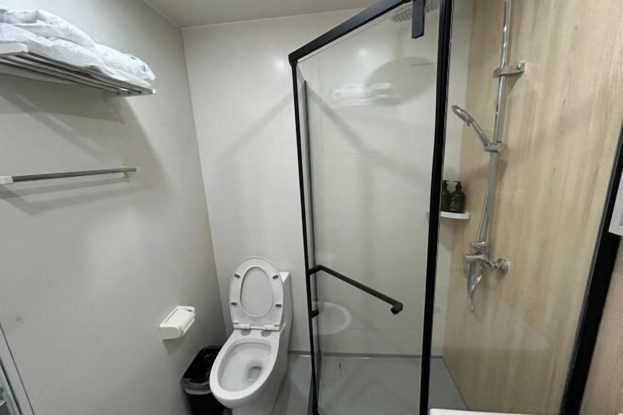 A small, modern bathroom with a glass shower enclosure, a white toilet, and a towel rack.