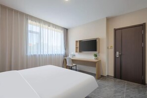 Ett hotellrum med en säng, ett skrivbord, en stol, en tv och en dörr.