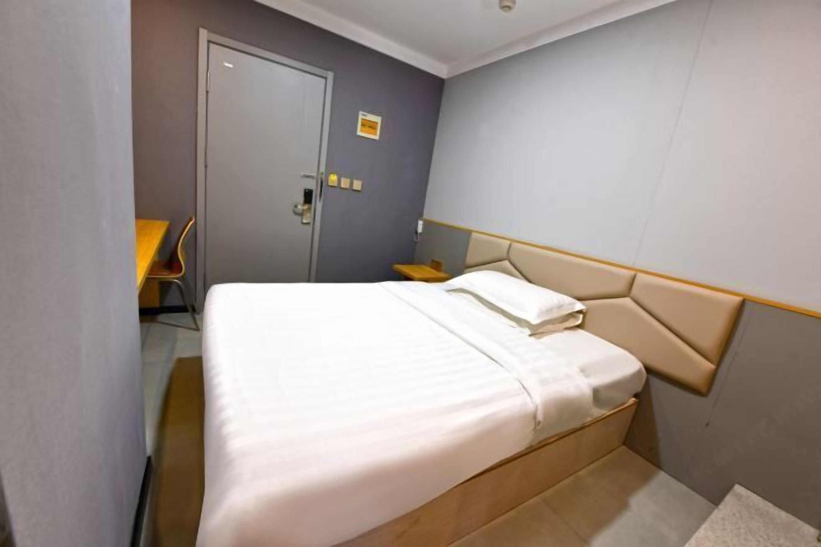 Ein Hotelzimmer mit einem Einzelbett, einer Tür, einem kleinen Tisch und einem Stuhl.