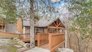A cabin with a stone exterior, wooden deck, and a stone staircase leading to the entrance.