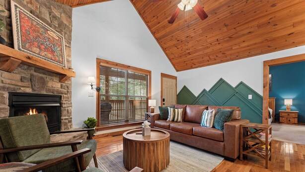 A cozy living room with a stone fireplace, wooden ceiling, and a green couch with patterned cushions.
