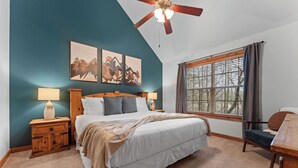 A bedroom with a large bed, wooden nightstands, a ceiling fan, and artwork on the walls.