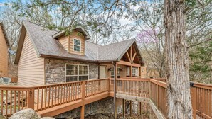 A cabin with a stone exterior, wooden deck, and a stone staircase leading to a porch.