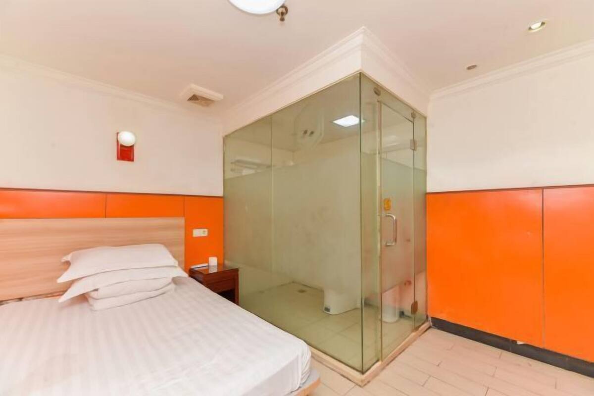 A hotel room with a bed, a glass-enclosed shower, and orange walls.