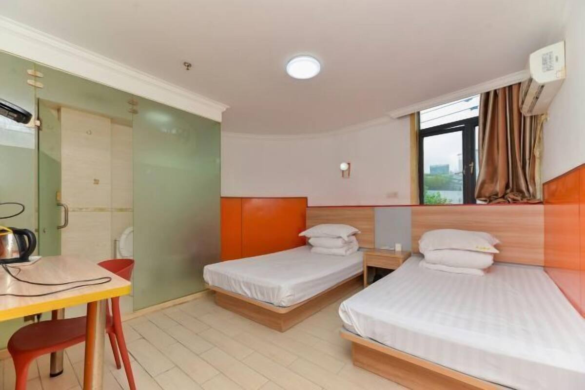 A hotel room with two single beds, a desk with a chair, and a window with curtains.