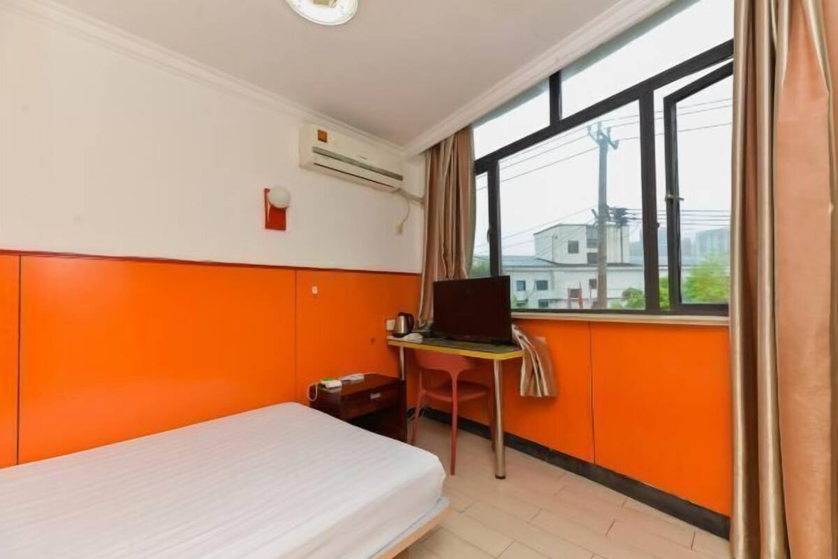 A room with a bed, a desk with a laptop, a chair, an air conditioning unit, and a window with curtains.