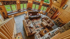 A spacious living room with a large sofa set, a coffee table, and a fireplace. There are multiple windows providing natural light and views of the outdoors.